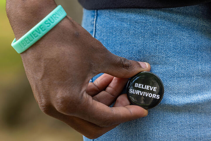 A close-up shot of a man's hand holding a button that says "Believe Survivors."